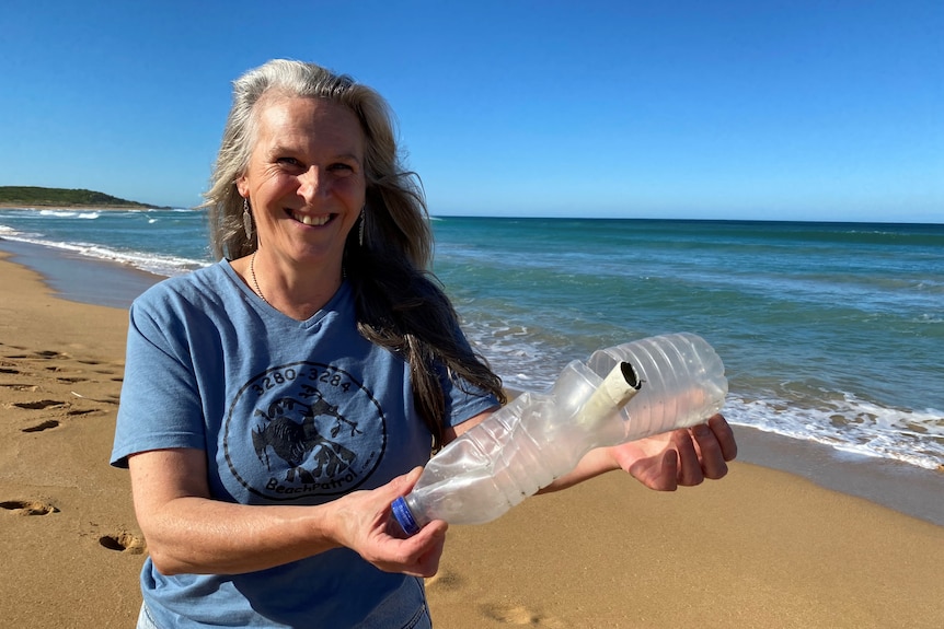 A smiling woman holds a bottle on a beautiful regional australian beach