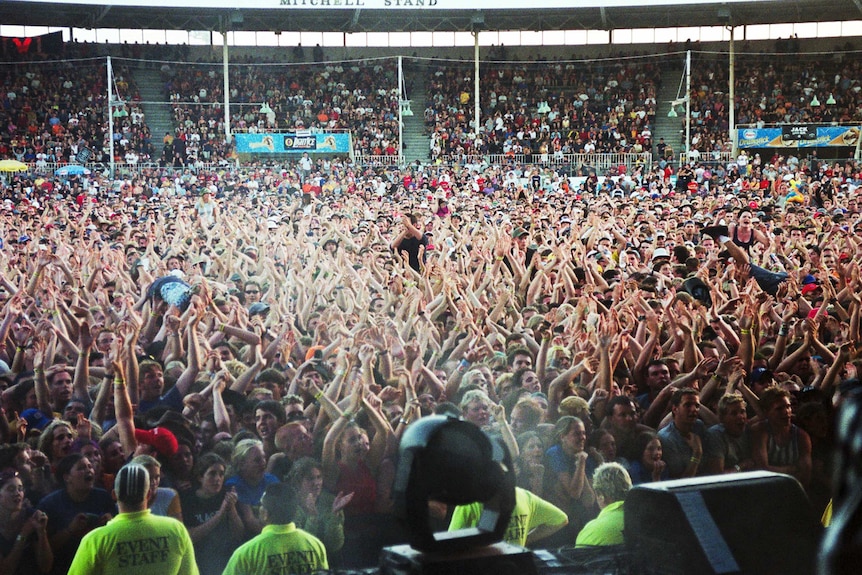 A sea of people with their hands in the air, with security in yellow shirts in the foreground