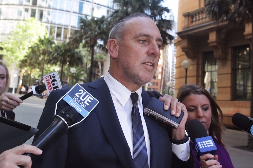 a man in suit surrounded by reporters