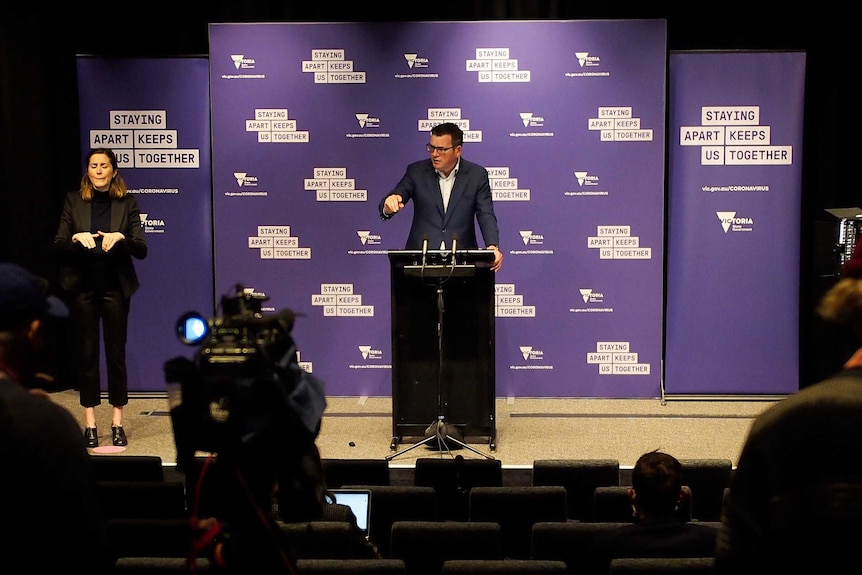 Daniel Andrews standing in front of a purple background next to an interpreter at a press conference.