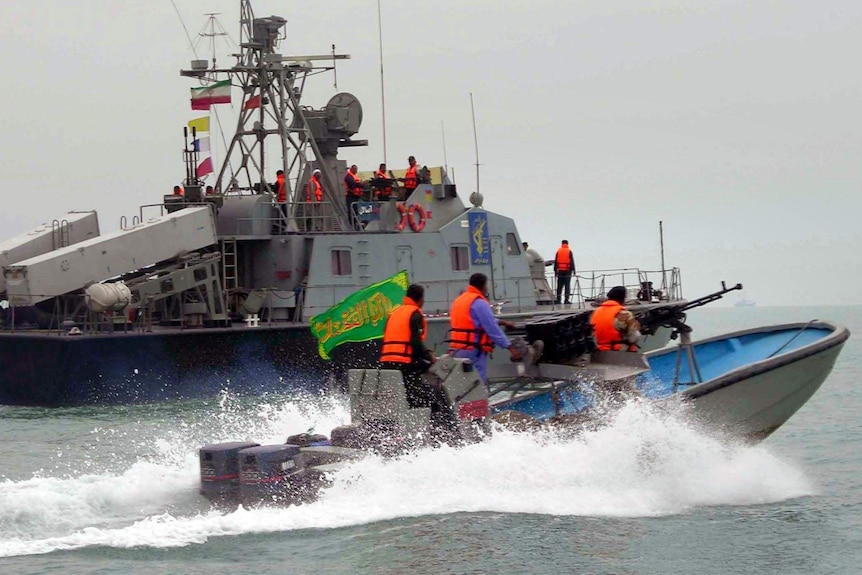 Iran's Revolutionary Guard, with guns, ride in their speed boat alongside a much larger Iranian naval vessel.