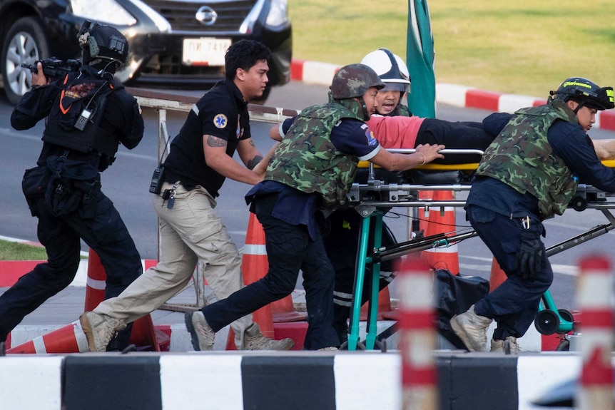 A man on a stretcher is pushed across a street as an armed soldier with a gun points his weapon away.