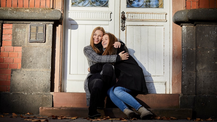 Two happy young women sitting on a doorstep hugging