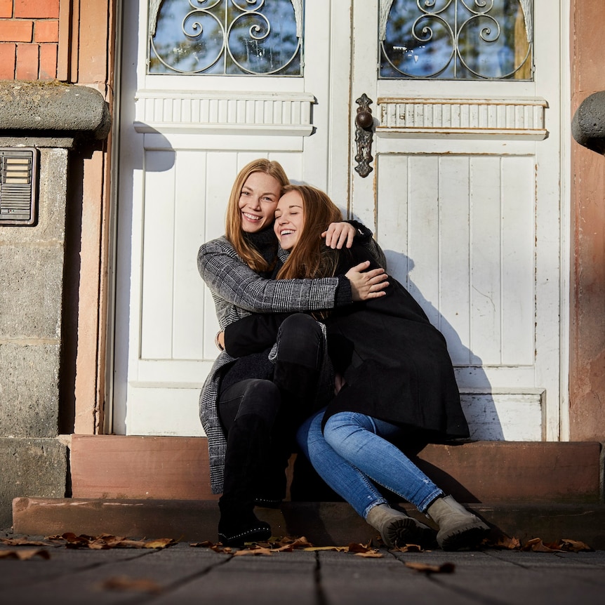 Two happy young women sitting on a doorstep hugging
