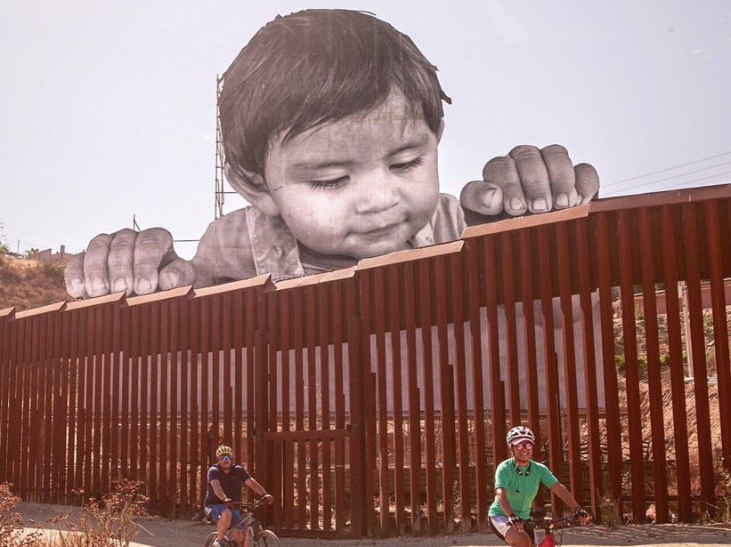 A large portrait of a baby peers over wall and appears to overlook two male cyclists