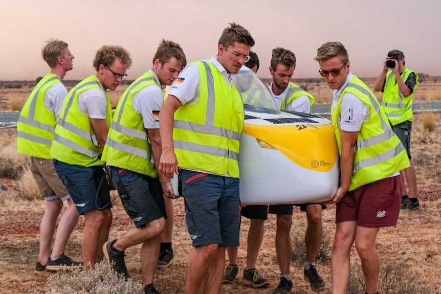 A group of men carry a solar vehicle
