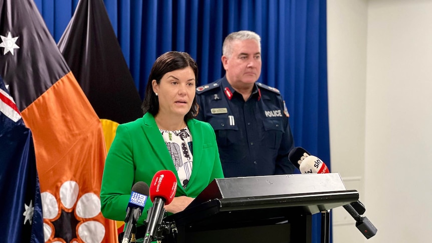 NT Chief Minister Natasha Fyles and a man in a NT Police uniform standing at a lectern inside a room.