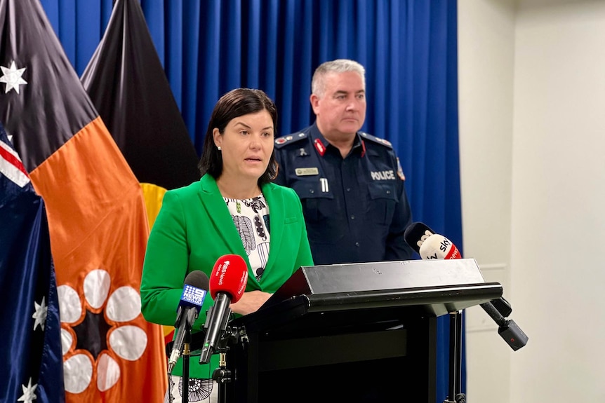 NT Chief Minister Natasha Fyles and a man in a NT Police uniform standing at a lectern inside a room.