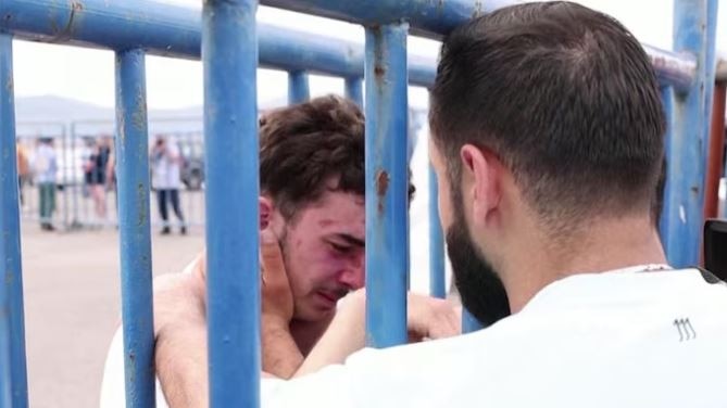 A man hugs another man who is behind bars and is crying.