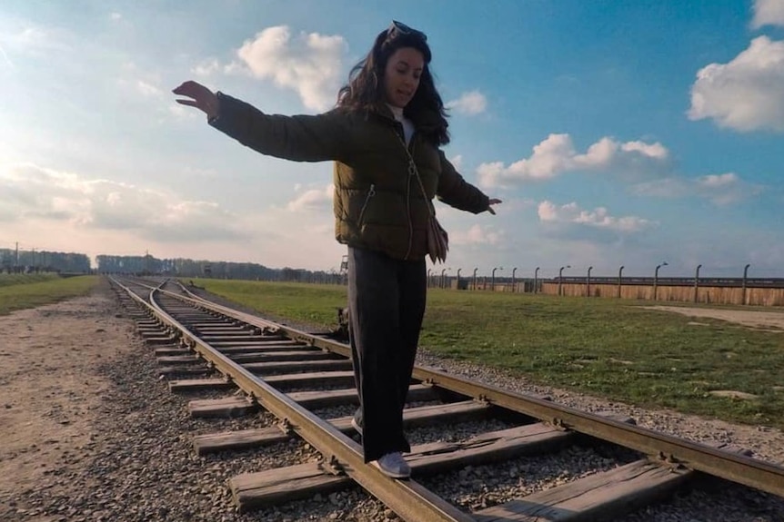A woman extends her arms as she balances on the rail of a train track, which leads to Auschwitz.