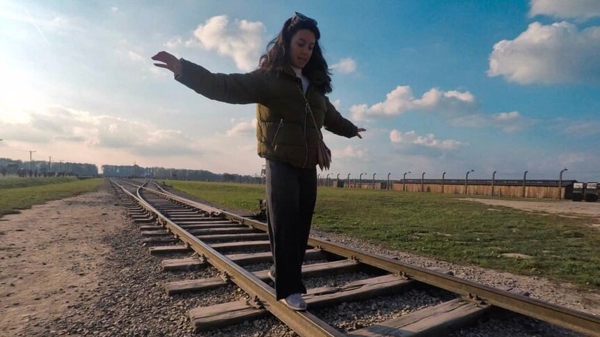 A woman extends her arms as she balances on the rail of a train track, which leads to Auschwitz.