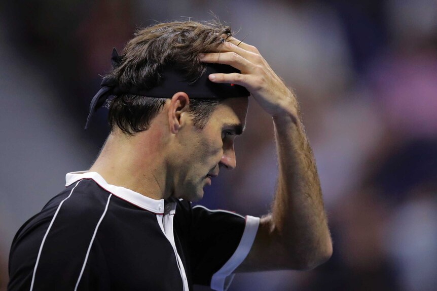 A male tennis player holds his head with his eyes closed after losing a point.