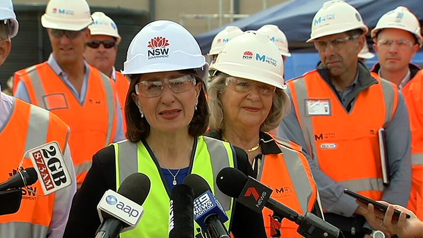A woman in a hard hat speaking behind microphones