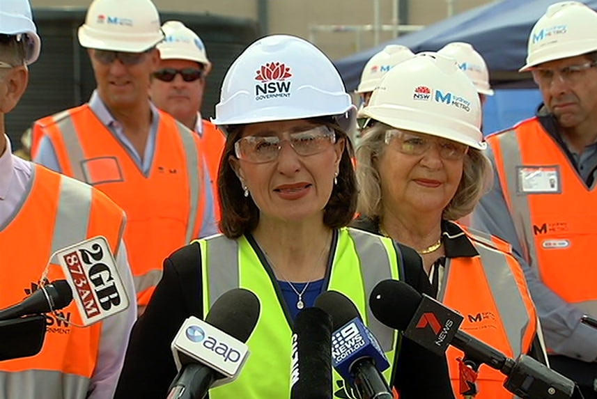 A woman in a hard hat speaking behind microphones