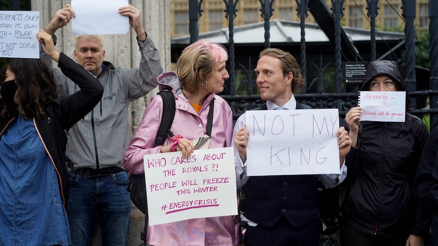 Paul stands with a 'not my king' sign and chats to another protester 