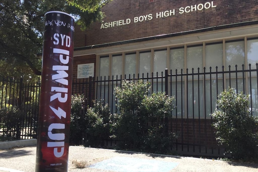 A black and red poster is wrapped around a yellow pole outside a school's brick building