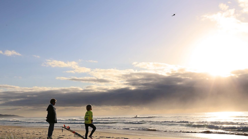 A junior competition surfer watches as a helicopter circles overhead