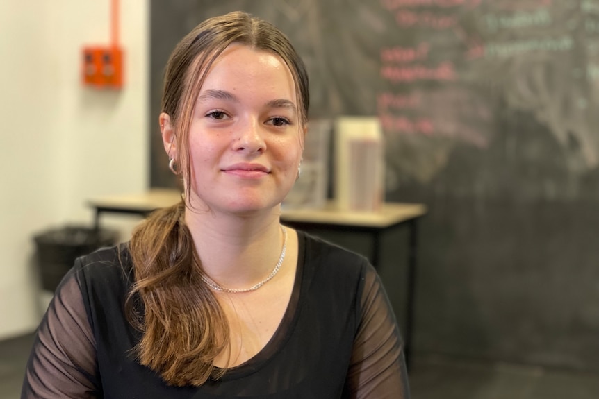 High school student Catie Owens wearing a black top, in a room with a chalkboard.