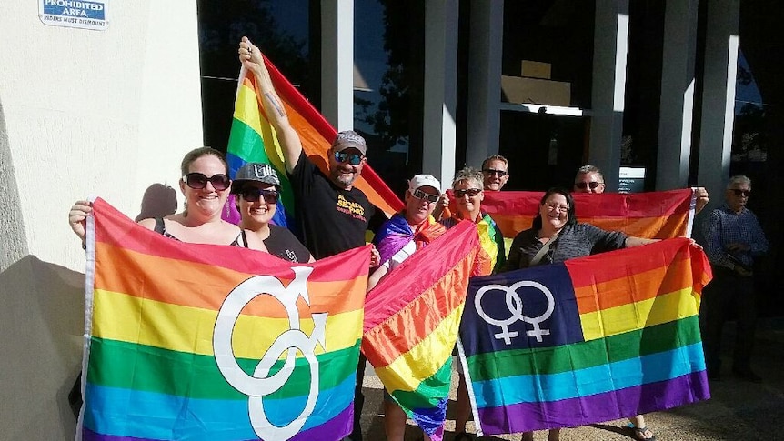 Eight people hold four rainbow flags outside SCRC council chamber at Nambour