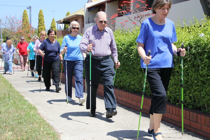 Older people walking in a line along the pavement with walking sticks