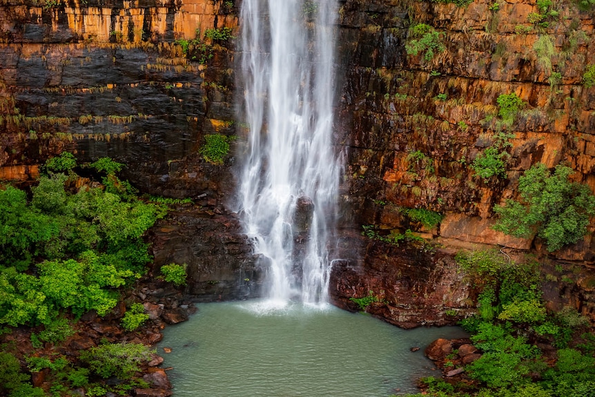 a waterfall flows down orange cliffs into a pool.