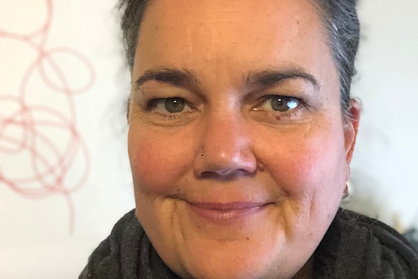 A woman with gray hair in a ponytail smiles at the camera while wearing a scarf.