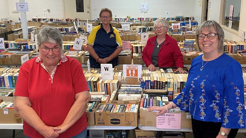 Four women stand in a room full of books.