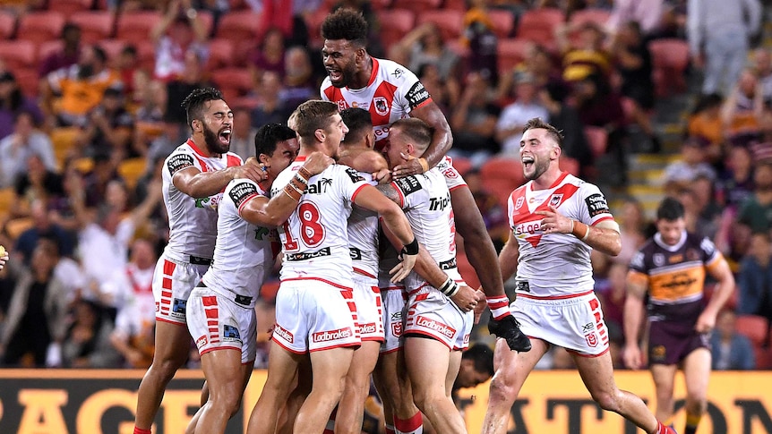 The Dragons jump on and hug Corey Norman after he kicked the winning field goal against the Broncos.