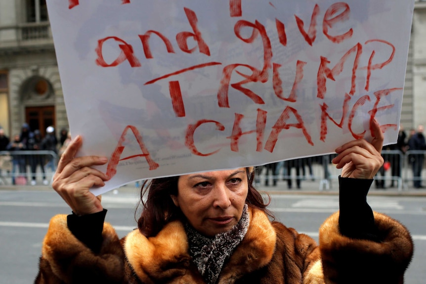 A woman holds a sign reading "give trump a chance"