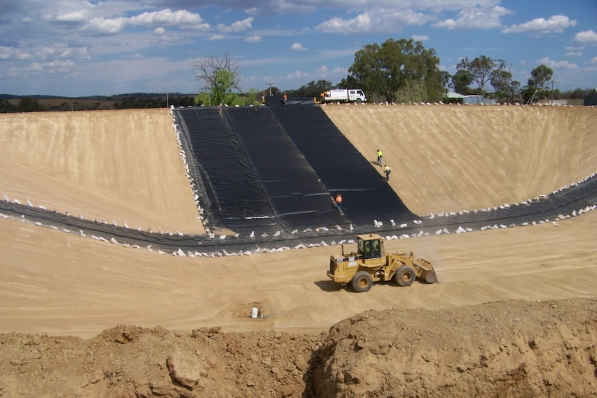 Bulldozer at the bottom of a large dam with workers laying black plastic lining around the dam walls at Young New South Wales