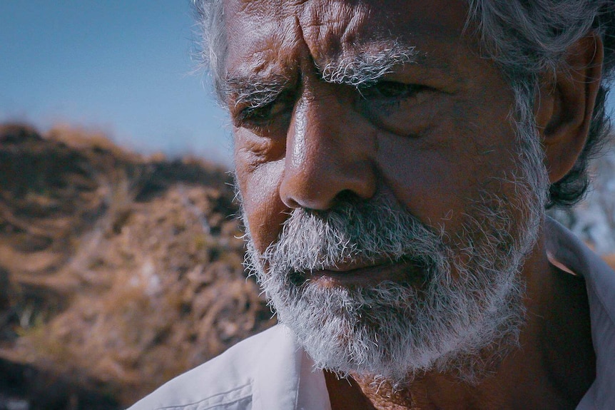 An older Aboriginal man staring off into the distance with a sorrow expression.
