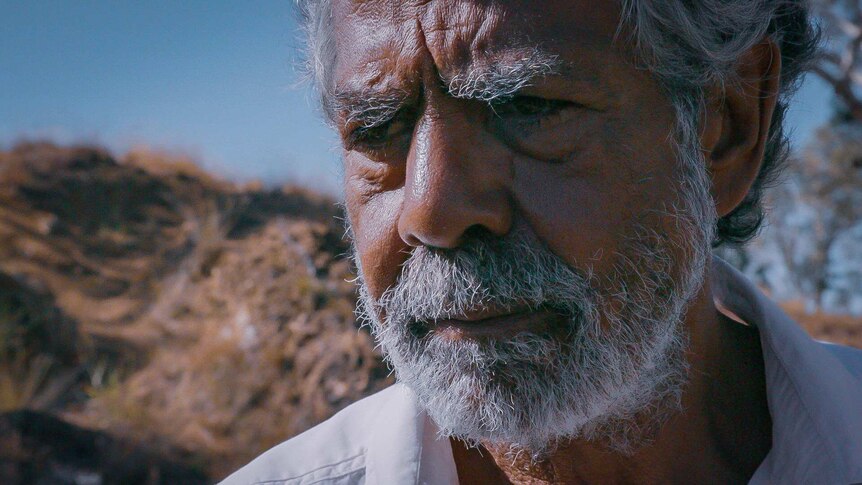 An older Aboriginal man staring off into the distance with a sorrow expression.