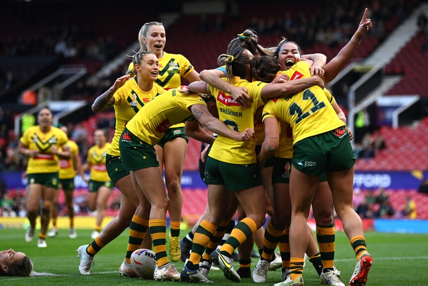 Women hug and smile while wearing yellow rugby kit