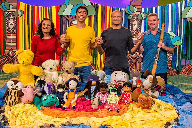 Miranda Tapsell, Hunter Page-Lochard, Luke Carroll and Matthew Doyle holding hands while standing behind the Play School toys