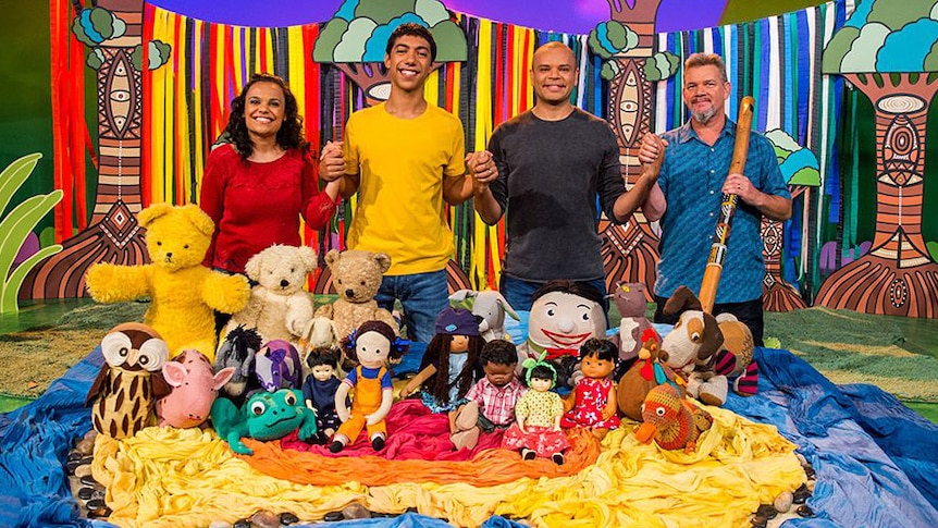 Miranda Tapsell, Hunter Page-Lochard, Luke Carroll and Matthew Doyle holding hands while standing behind the Play School toys
