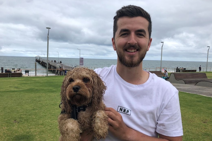 A man standing near an Adelaide beach holding his dog