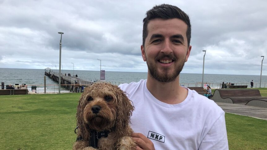 A man standing near an Adelaide beach holding his dog