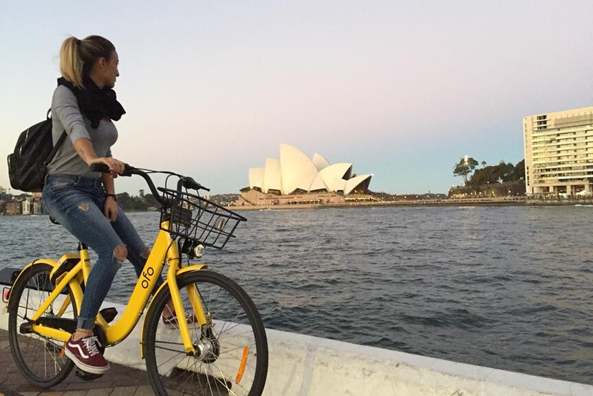 French backpacker Ludmilla Cek sitting on a bike looking across Circular Quay to the Opera House.