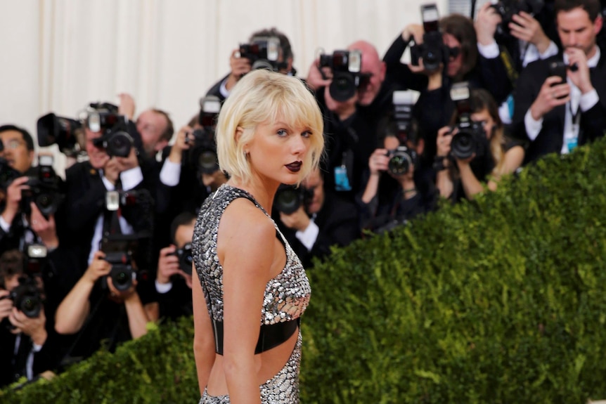 Taylor Swift in bleached blonde hair walks up the red carpet in a silver dress.