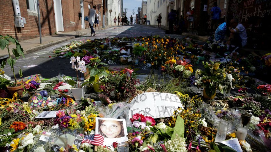 A photo of Heather Heyer lies on the street amid flowers and a sign saying "No place for hate".