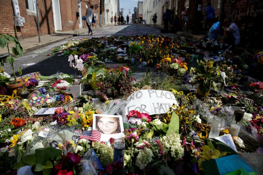 A photo of Heather Heyer lies on the street amid flowers and a sign saying "No place for hate".