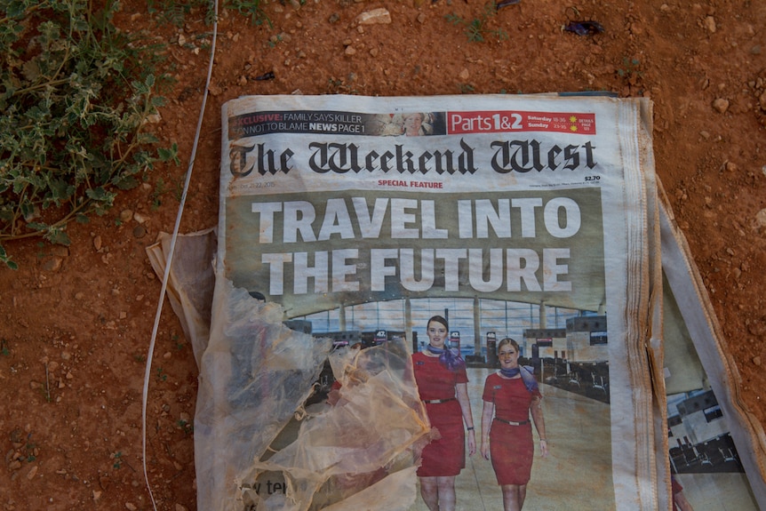 A muddy newspaper lying in red dirt.