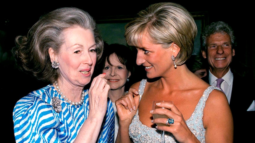 A woman with a bouffant chats to a blonde woman in a pale blue evening gown