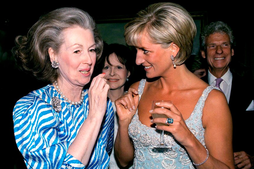 A woman with a bouffant chats to a blonde woman in a pale blue evening gown