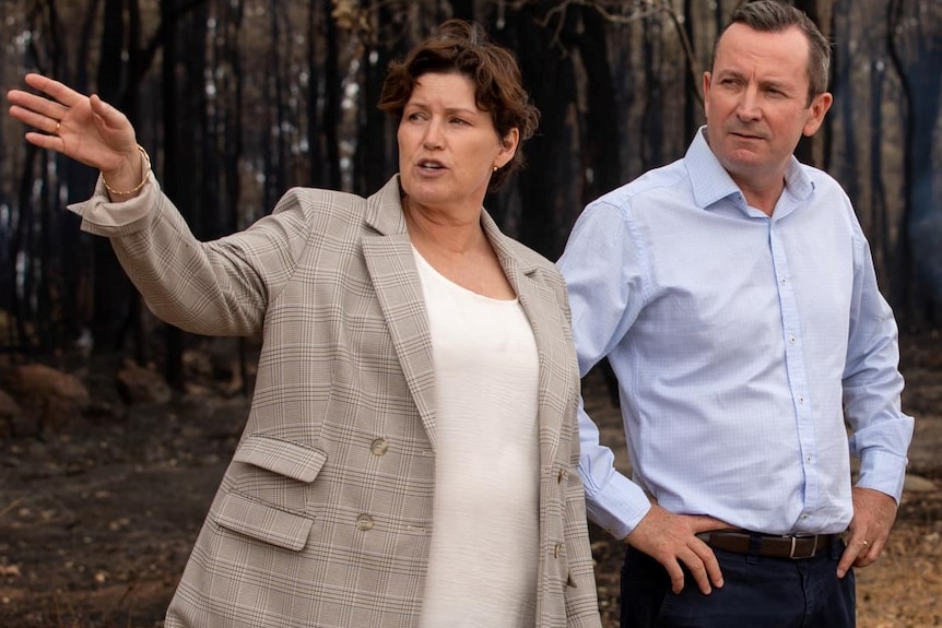 Une femme aux cheveux noirs fait des gestes alors qu'elle se tient dans une forêt à côté du premier ministre de WA, Mark McGowan.