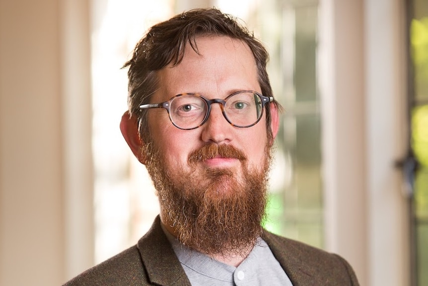 A bearded man wearing glasses poses for a portrait