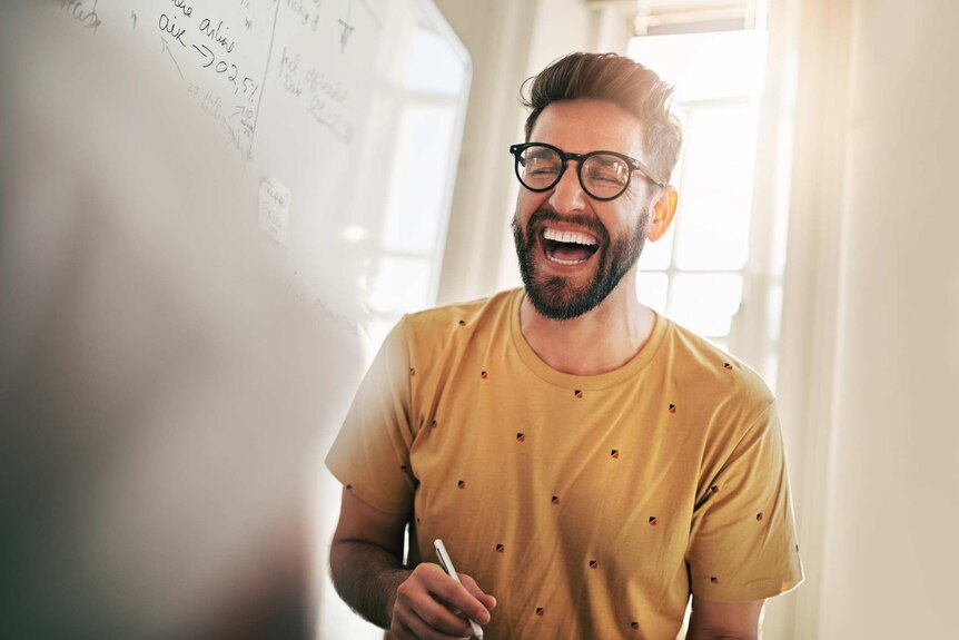 Man laughs in front of a whiteboard in an office.