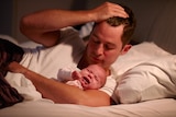 A man holding a crying baby in bed
