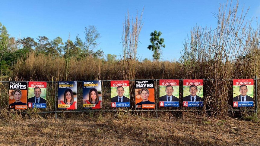 NT election corflutes on a fence with some gamba grass behind.