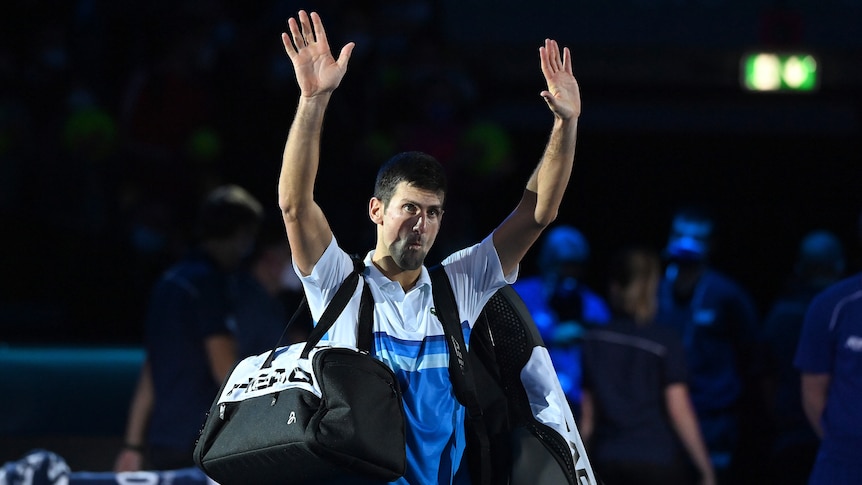 A tennis player holds his hands above his head in salute and a farewell to the crowd after losing a match.